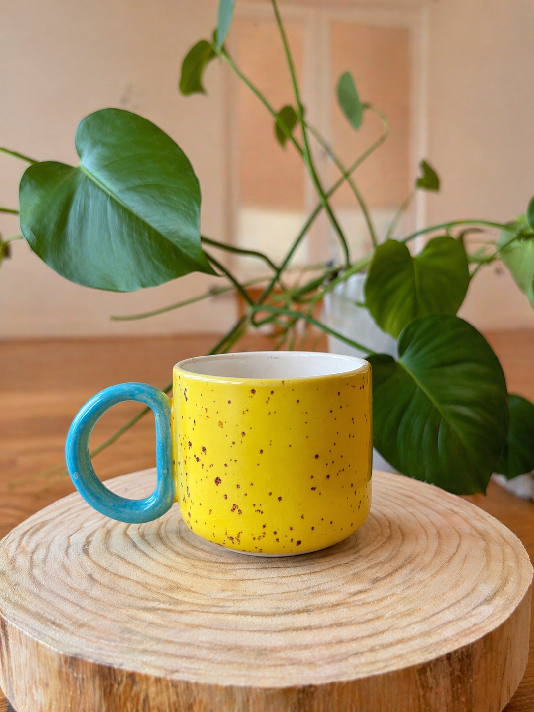 Žlutý keramický hrnek s modrým uchem na dřevěné podložce